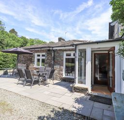 A stone cottage with patio furniture and an umbrella outside at Rowan Cottage in Grasmere