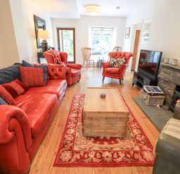 A living room with red leather sofas and armchairs a wooden coffee table a fireplace and a television at Rowan Cottage in Grasmere