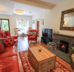 A living room with red leather sofas a wooden chest table a fireplace and a television at Rowan Cottage in Grasmere