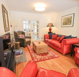 A living room with red leather sofas a wooden coffee table and glass doors at Rowan Cottage in Grasmere