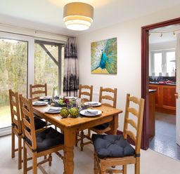 A dining room with a wooden table and six chairs next to sliding glass doors and a kitchen visible through an open door at Beech View in Ambleside