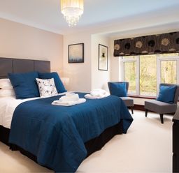 A bedroom with a bed blue bedding two chairs and a window at Beech View in Ambleside