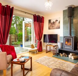 A living room with a wood-burning stove red curtains open glass doors and wooden furniture at Artists Hideaway in Keswick