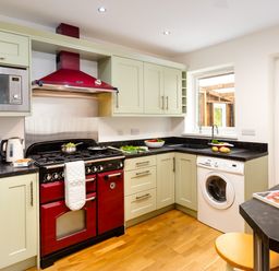 A kitchen with red stove and hood green cabinets washing machine and wooden floor at Artists Hideaway in Keswick