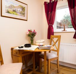 A small dining area with a wooden table and chairs a vase with flowers on the table and red curtains by the window at Artists Hideaway in Keswick
