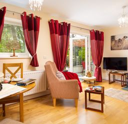 A living room with red curtains a striped armchair a television and a wood burning stove at Artists Hideaway in Keswick