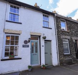 Front view of a white cottage with green door and windows with flowers at Tizzie Whizie Cottage in Windermere