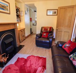 A living room with a fireplace wooden furniture two leather chairs and a sofa with cushions at Tizzie Whizie Cottage in Windermere