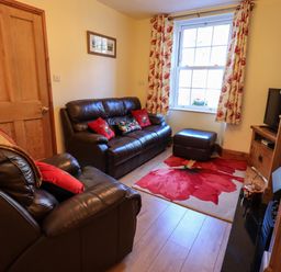 A sitting room with leather armchairs and sofa a floral rug and curtains near a window at Tizzie Whizie Cottage in Windermere
