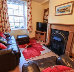 A sitting room with leather sofas a fireplace a television floral curtains and a red floral rug at Tizzie Whizie Cottage in Windermere