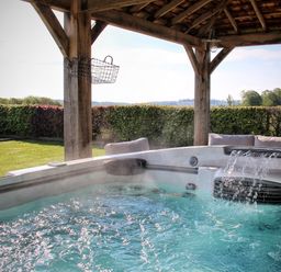An outdoor hot tub with water flowing under a wooden gazebo with a lawn and hedge in the background at Hawkrigg Farm in Hawkshead
