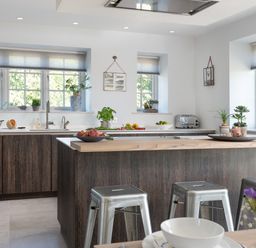 A kitchen with wooden island, metal stools, sink, countertop with fruit bowls and plants at Hawkrigg Farm in Hawkshead