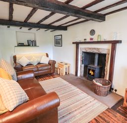 A living room with leather sofas a rug a wood burning stove and wooden beams on the ceiling at Blease Garth in Threlkeld