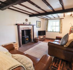 A living room with wooden beams on ceiling a fireplace with wood burner two leather sofas a television and a window at Blease Garth in Threlkeld