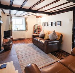 A living room with brown leather sofas a rug a television and framed pictures on the wall at Blease Garth in Threlkeld