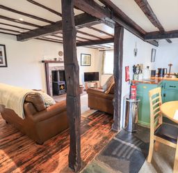 An open plan living room and kitchen with exposed wooden beams and leather sofas at Blease Garth in Threlkeld