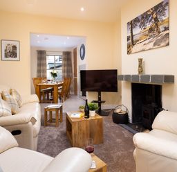 A living room with beige leather sofas a wooden coffee table and a television next to a fireplace at Dovedale in Keswick
