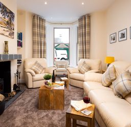 A living room with cream sofas wooden tables fireplace and bay window at Dovedale in Keswick