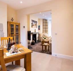 A dining area with a wooden table set for four with wine glasses and a bottle and an adjoining living room with armchairs and a fireplace at Dovedale Keswick