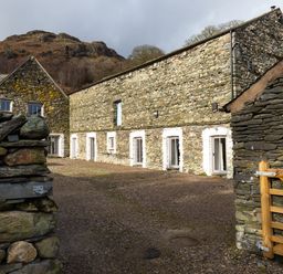 A stone walled building with multiple white framed doors and windows and a wooden gate in the foreground at Kentmere Hall Bank Barn in Kentmere