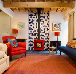 A living room with a red armchair a blue sofa and a red wood stove with hexagon tiles at Kentmere Hall Bank Barn in Kentmere