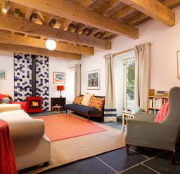 A living room with wooden ceiling beams red stove blue couch beige armchair and bookshelves at Kentmere Hall Bank Barn in Kentmere