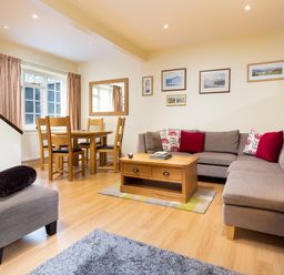 A living room with a gray sectional sofa a wooden coffee table a dining table with chairs and wall art at Scots Pine in Keswick