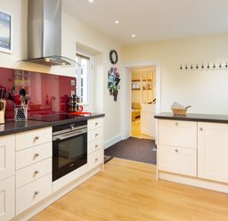 A kitchen with white cabinets a built in oven a stove with a stainless steel hood and a red backsplash at Scots Pine in Keswick