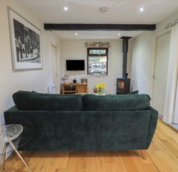 A living room with a green sofa a wood burning stove wooden floor and a TV at Corner Cottage in Troutbeck