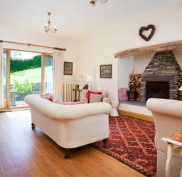 A living room with two white sofas a stone fireplace and a glass door showing a garden at The Old Coach House in Troutbeck