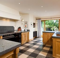 A kitchen with wooden cabinets checkered floor and large glass doors showing a garden at The Old Coach House in Troutbeck