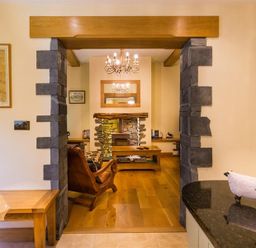 A view from a kitchen with black countertop and sheep figurines to a living room with stone fireplace wooden coffee table and armchair at Oaklea in Ambleside