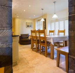 A dining area with a wooden table covered with a polka dot tablecloth and wooden chairs next to windows with shutters at Oaklea Ambleside