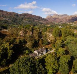 A house surrounded by trees with mountains in the background at Oakbank in Langdale