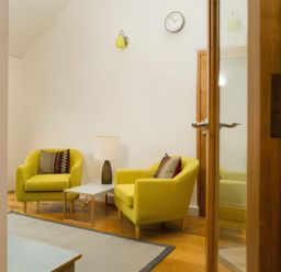 A room with two yellow armchairs a small table with a lamp a wall clock and a wooden floor at Oakbank Langdale
