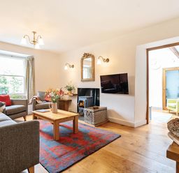 A living room with grey sofas a wooden coffee table a red and blue rug a wood burning stove and a wall-mounted TV at Oakbank in Langdale