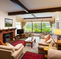 A living room with sofas a coffee table a fireplace and large windows overlooking a garden at Lakefield House in Hawkshead