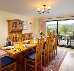 A dining room with wooden table and chairs set with plates and fruit and sliding glass door opening to outdoor seating at Lakefield House in Hawkshead