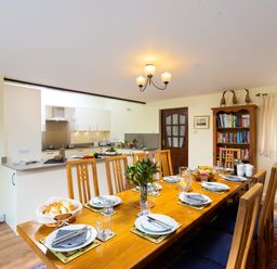A dining room with a wooden table set for a meal next to a kitchen and bookshelf at Lakefield House in Hawkshead