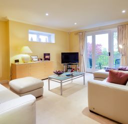 A living room with white sofas a glass coffee table and a TV near a balcony at Merewood Lodge in Ambleside