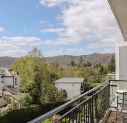 A balcony with table and chairs overlooking trees buildings and hills at The Heights in Bowness
