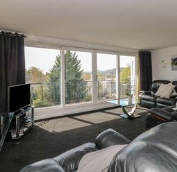 A living room with leather sofas a glass coffee table a television and large windows with a view at The Heights in Bowness