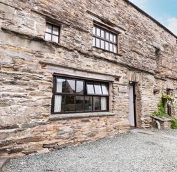 Stone exterior wall of a cottage with windows doors and gravel driveway at Cherry Tree Cottage at Satterthwaite in Hawkshead