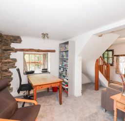 A room with a wooden table and chairs stone wall accents and a bookshelf near a staircase at Cherry Tree Cottage at Satterthwaite in Hawkshead