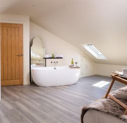 A bathroom with a freestanding bathtub wooden door sloped ceiling and skylights at Old Wool Loft in Ambleside