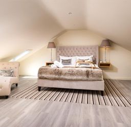 A bedroom with a bed and two bedside lamps a chaise lounge and a table lamp at Old Wool Loft in Ambleside