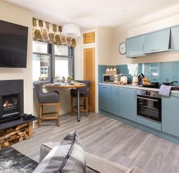 A kitchen with blue cabinets a dining table with chairs a wall-mounted TV and a fireplace at Old Wool Loft in Ambleside