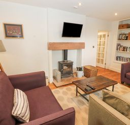A living room with sofas a coffee table a fireplace with a mounted television and a bookshelf at Home Farm House in Penrith