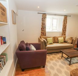 A sitting room with two purple armchairs a brown sofa a wooden coffee table bookshelves and a window with patterned curtains at Home Farm House Penrith