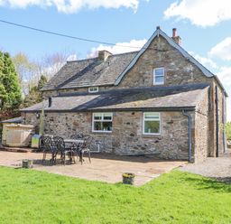 Stone house with patio furniture and a wooden hot tub in a garden at Home Farm House in Penrith